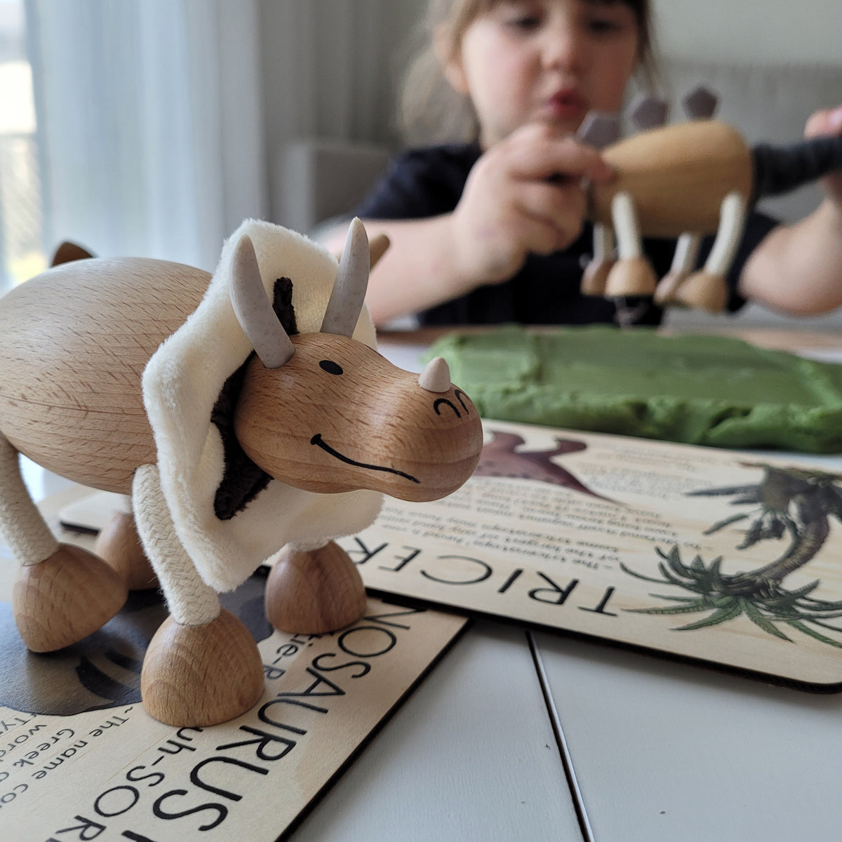 wooden dinosaur toy on a table with a small girl in the background playing another wooden dinosaur toy